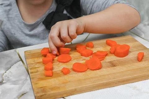 Child's small hands master knife techniques with soft carrots under adult s.. Stock Photos