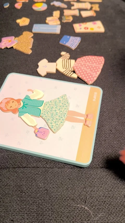 A childs small hands pick up and apply magnetic clothing elements to a picture Stock Footage 327824462