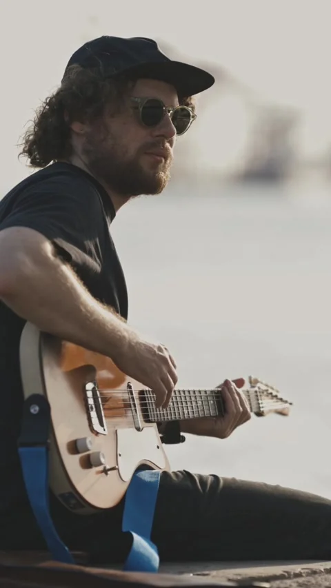 Chill young man playing guitar on the embankment in the city Stock Footage 328421357