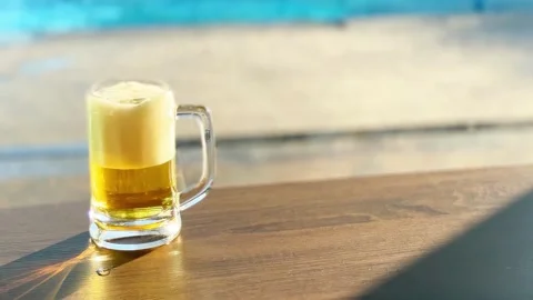 Chilled beer with a frothy head sits on a sunlit table Stock Footage 274087459