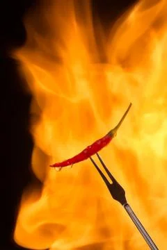 Chilli pepper on meat fork with flame behind on black background 写真素材