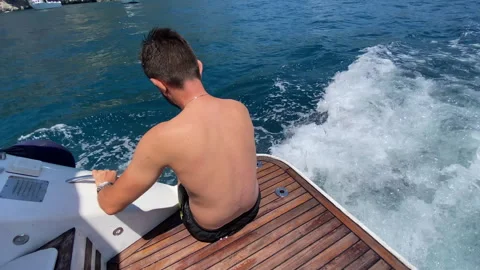 Chilling man sitting on aft deck of sailing motorboat with legs put inside the Stock-Footage 318648644