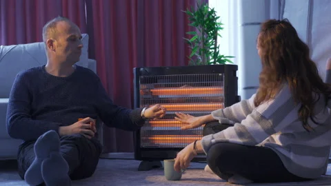 The chilly couple are warming themselves by the electric heater. Vídeo Stock 220659651