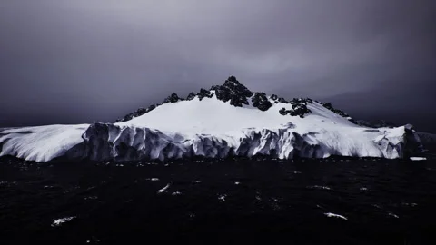 Chilly glacier plain extends beneath gloomy cloudy sky meeting deep dark sea Stock Footage 331396387