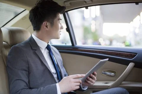  Chinese businessman using digital tablet in car back seat Beijing China C... Stock Photos