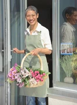 Chinese florist holding basket of flowers in doorway Stock Photos