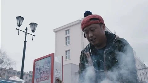 Chinese guy in a funny cap with a pompon prepare food on the street Stock Footage 73851812