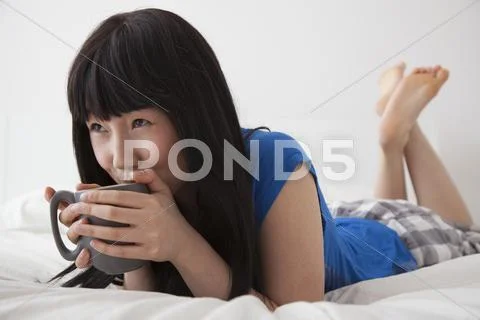 Chinese woman drinking cup of coffee on bed Stock Photos