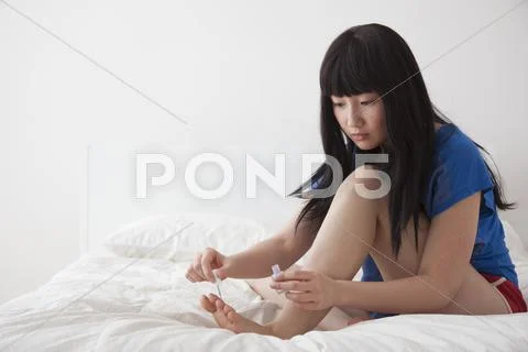 Chinese woman painting toenails on bed Stock Photos