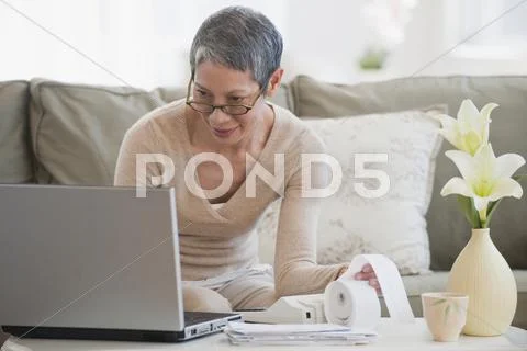 Chinese woman paying bills with laptop in living room Stock Photos