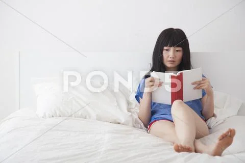 Chinese woman reading book on bed Stock Photos