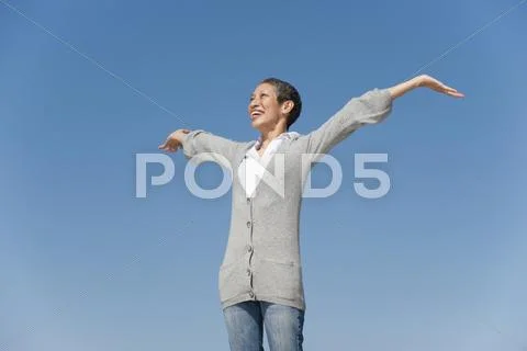 Chinese woman smiling with arms outstretched against blue sky Stock-Fotos