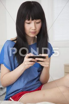 Chinese woman using cell phone on bed Stock Photos