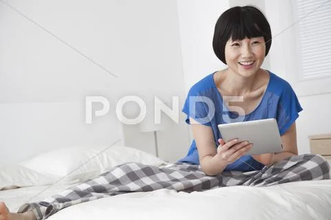 Chinese woman using tablet computer on bed Stock Photos
