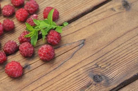 A chip of mint lies among the raspberry berries on the left on a wooden Stock Photos
