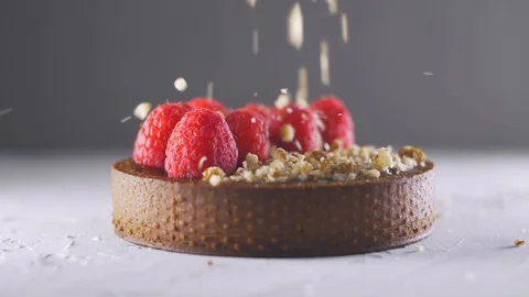 Chipped nuts falling down to the chocolate tart with raspberries and nuts Stock Footage 127644004