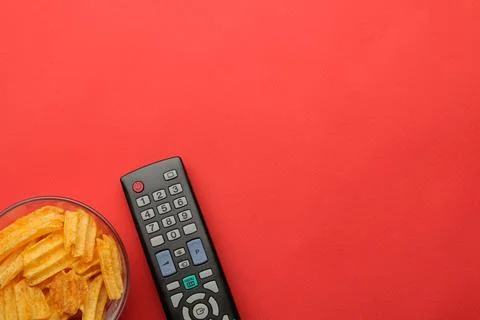 Chips and tv remote control on a bright red background. Concept of watching a Stock Photos