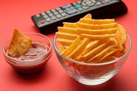 Chips and tv remote control on a bright red background. Concept of watching a Stock Photos