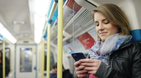 Chirpy young woman using her phone on a subway train, in slow motion Stock Footage