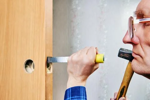 Chisel driven by hammer, cuts into wooden door frame to create mortise, wit.. Foto stock