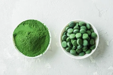 Chlorella or spirulina in the form of tablets and powder on a gray concrete b Stock Photos