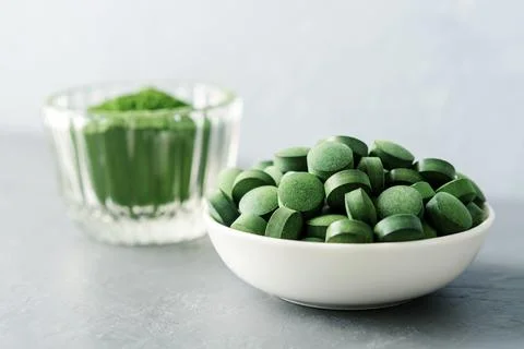 Chlorella or spirulina in the form of tablets and powder on a gray concrete b Stock Photos