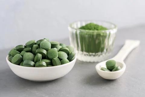 Chlorella or spirulina in the form of tablets and powder on a gray concrete b Foto stock