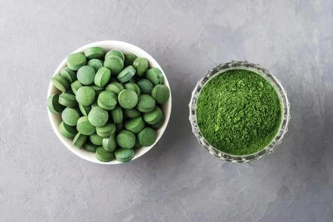 Chlorella or spirulina in the form of tablets and powder on a gray concrete b Photos