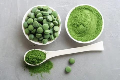 Chlorella or spirulina in the form of tablets and powder on a gray concrete b Stock Photos