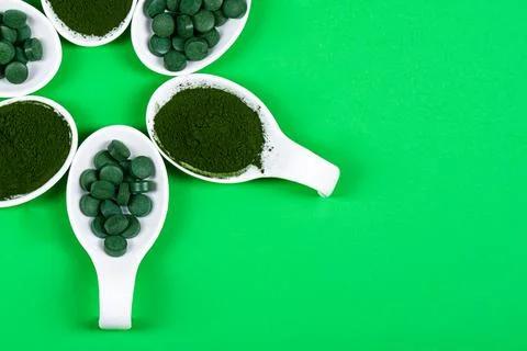 Chlorella or spirulina in the form of tablets and powder on a green backgroun Stock Photos