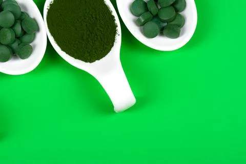 Chlorella or spirulina in the form of tablets and powder on a green backgroun Stock Photos