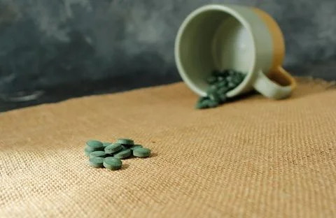 Chlorella or spirulina tablets falling out of mug Stock Photos
