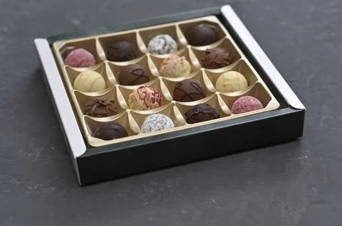 Chocolate assortment shown at angle in open box on dark surface. Stock Photos