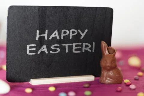 Chocolate bunny missing a bite and blackboard with the text Happy Easter Foto stock
