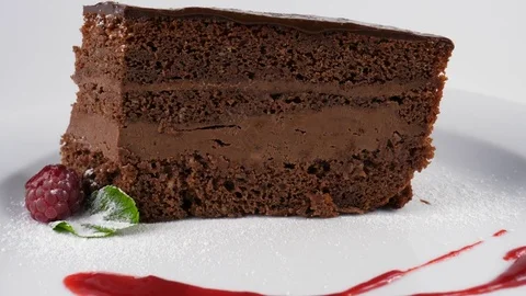 Chocolate cake decorated with raspberry, icing sugar, mint leaf and red jam Stock Footage 79985773