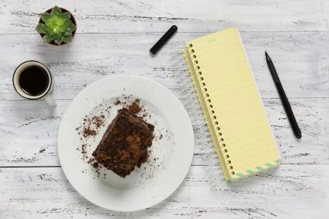Chocolate cake, empty yellow notebook, coffee on wooden background Stock Photos