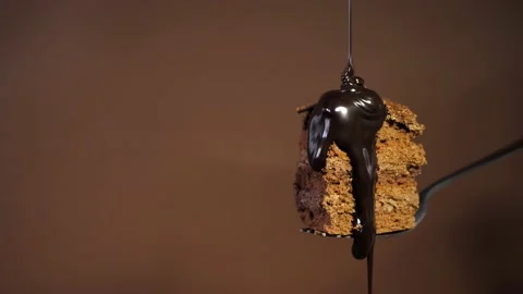 Chocolate cake on a fork is poured with chocolate sauce on a brown background. Stock Footage 236842810