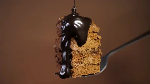 Chocolate cake on a fork is poured with chocolate sauce on a brown background Stock Footage 236908876