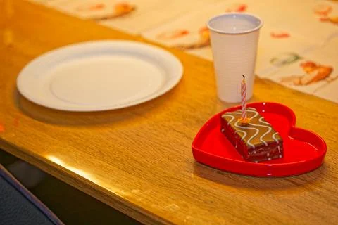Chocolate cake slice with candle on red heart shaped plate on wooden table Stock Photos
