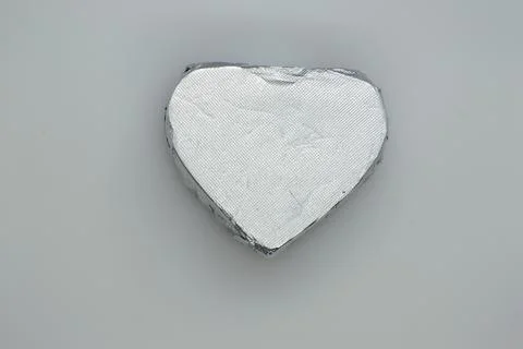 Chocolate candy wrapper in silver color. Heart shape on a gray background. 스톡 사진