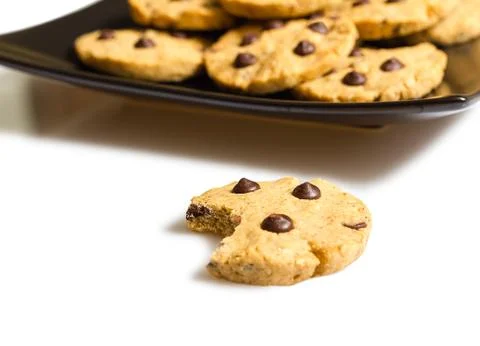 Chocolate chip cookie with a bite and pile of cookies in a plate on the backg Stock Photos