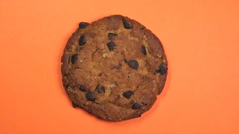 Chocolate chip cookie close-up, macro shot, slowly spinning on a rotating orange Stock Footage 89309002