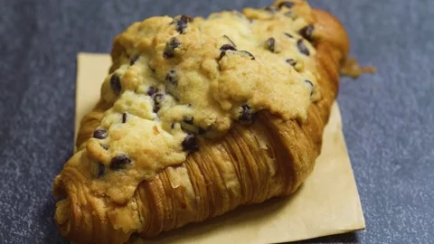 Chocolate chip cookie crookie crowning flaky croissant, sitting on rustic brown Stock Footage 314210564