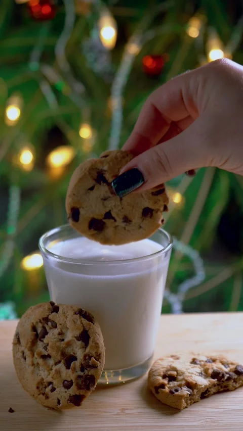 Chocolate chip cookie dipped into milk near festive Christmas tree. Stock Footage 293498195