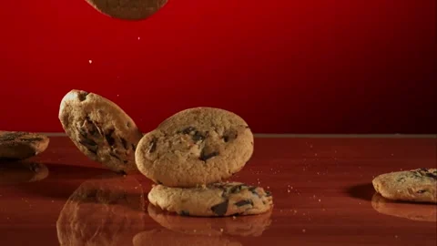 Chocolate chip cookies fall and stack up on a red reflective table. Stock Footage 326747702