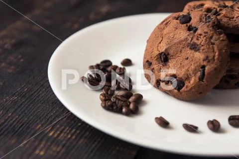 Chocolate chip cookies on a white plate with coffee beans on dark wooden tabl Stock Photos
