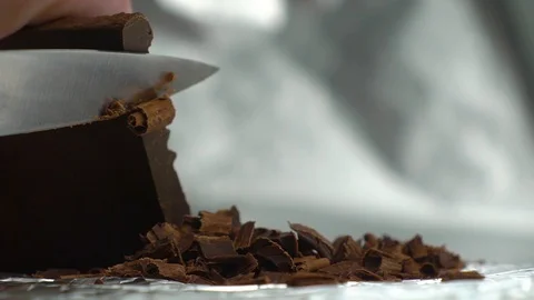 Chocolate chips cut with a sharp knife from a bar of chocolate on a silver Stock Footage 124133655