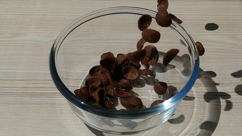 Chocolate cornflakes falling into empty transparent glass bowl, slow motion Stock Footage 96976386