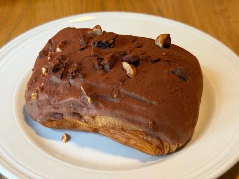 Chocolate-covered pastry with nuts on white plate. Sweetness, texture, and .. Stock Photos