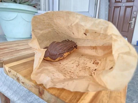 Chocolate-Covered Pastry in Open Paper Bag on Wooden Surface Foto stock